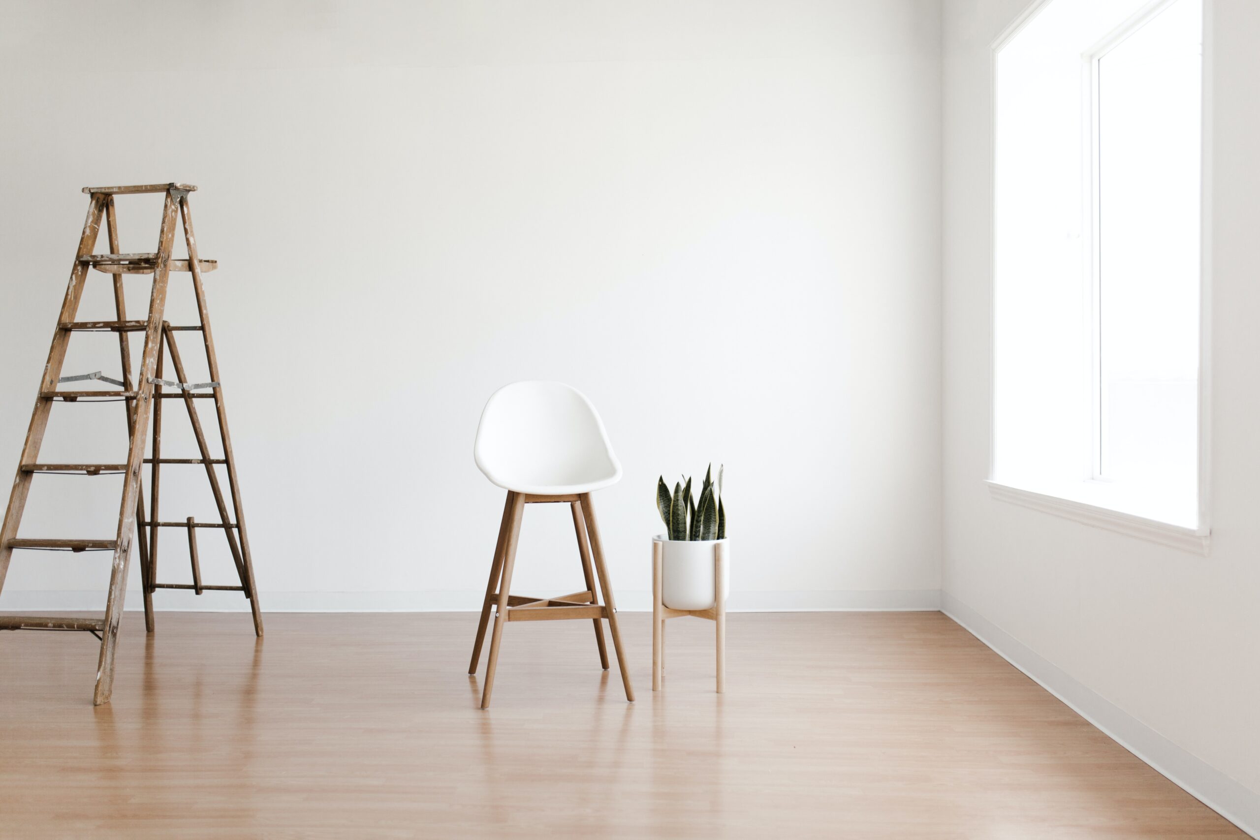 room with white walls, ladder, chair and plant